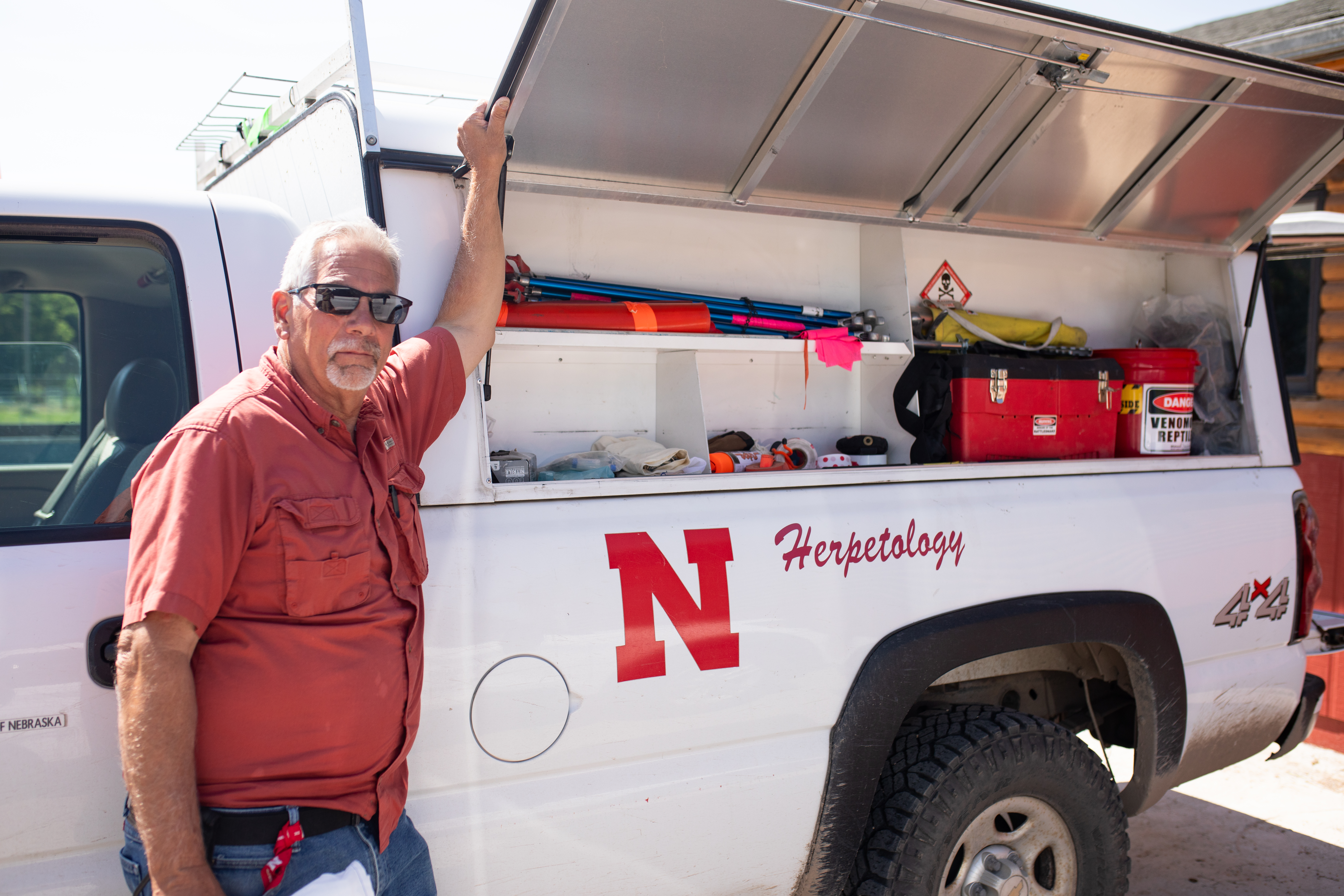 White truck with open storage containing field equipment, labeled "Herpetology," parked outdoors.